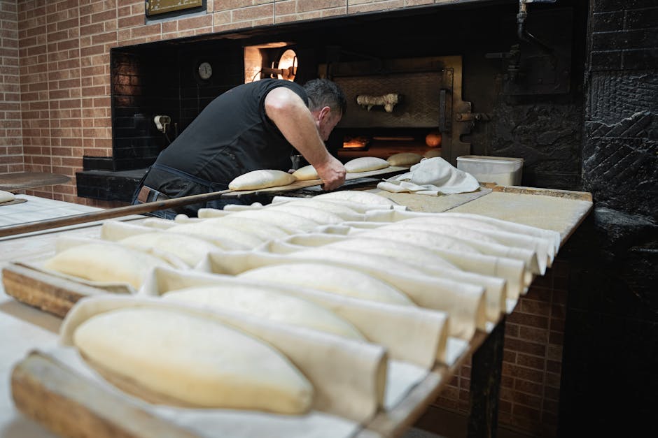Traditional baker placing dough into a rustic oven in a bakery.