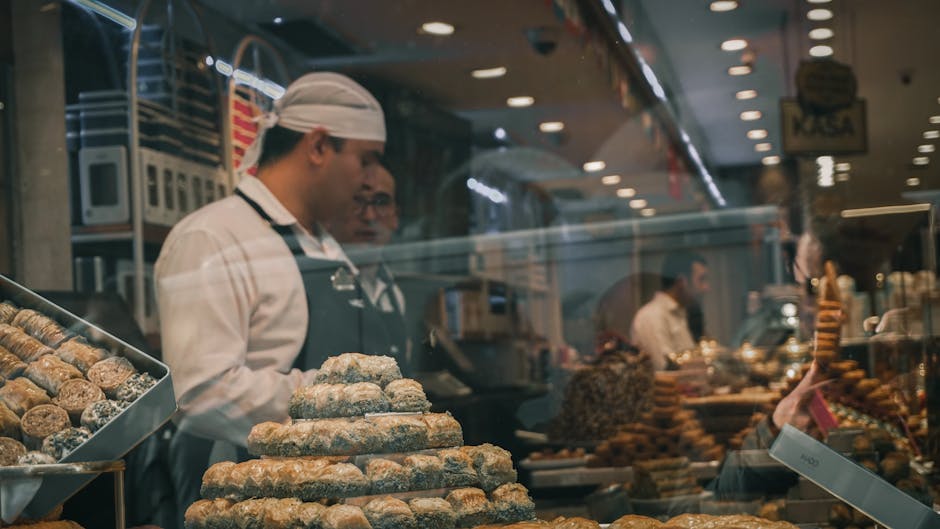 Two bakers working inside a bakery with a display of assorted pastries and sweets.