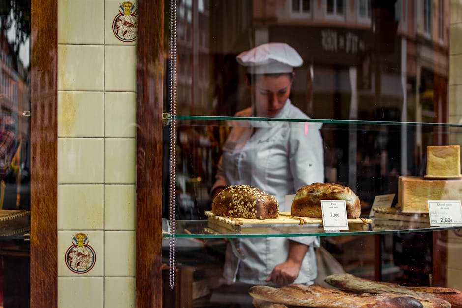 Chef behind a bakery window showcasing gourmet breads on glass shelves.