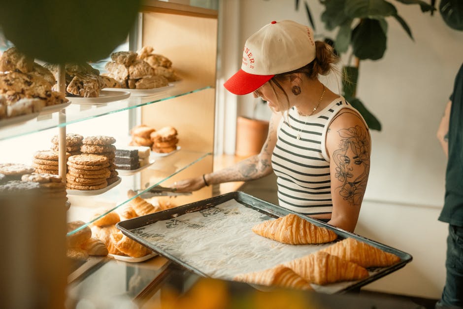 A pastry chef in a bakery arranges croissants, showcasing an inviting display of cookies and croissants.